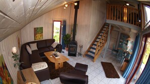 A cozy living room with a sofa, coffee table, and ottoman, a fireplace, a staircase, and a dining area with chairs and a table. - Sunny Danish cottage44. de am See in the holiday park Mirow (Granzow)