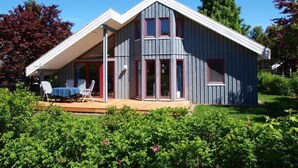 A two-story house with a sloped roof, large windows, and a covered porch with outdoor seating. - Sunny Danish cottage44. de am See in the holiday park Mirow (Granzow)