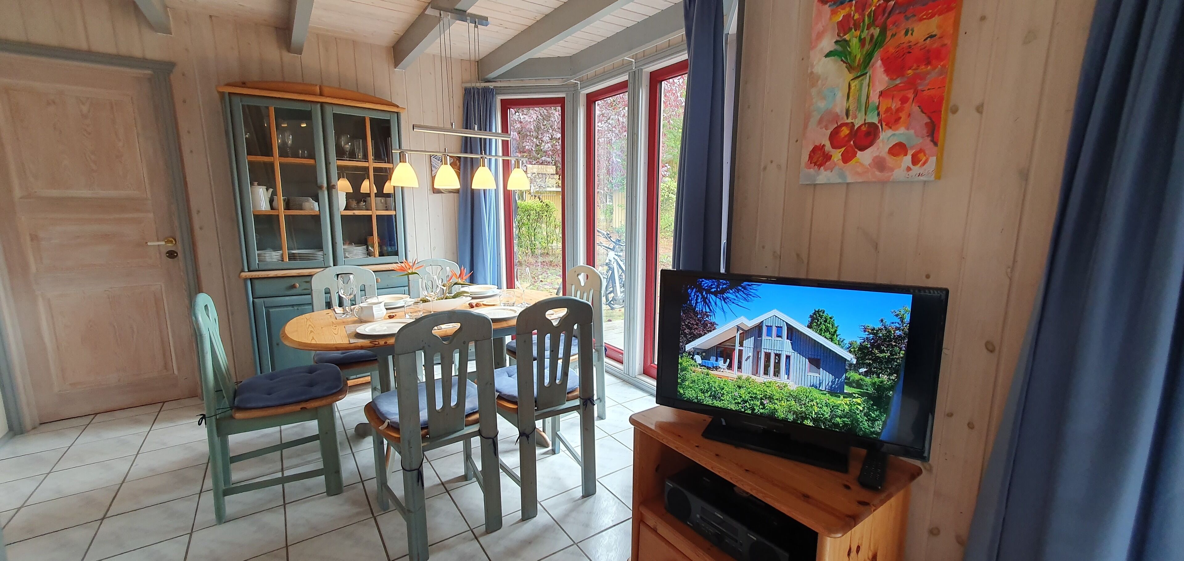 Un coin repas avec une table en bois, des chaises et un téléviseur qui diffuse une image d’une maison.
