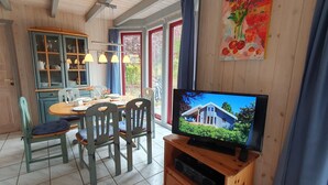 A dining area with a wooden table, chairs, and a television displaying a house. - Sunny Danish cottage44. de am See in the holiday park Mirow (Granzow)