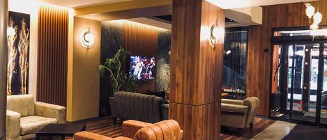A modern lobby with a seating area, a TV screen, and a wooden reception desk.