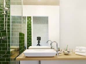 A modern bathroom with a white sink, a handheld showerhead, a tripod-mounted camera, and a glass of water on the counter. - ipartment Cologne Mülheim (Cologne)