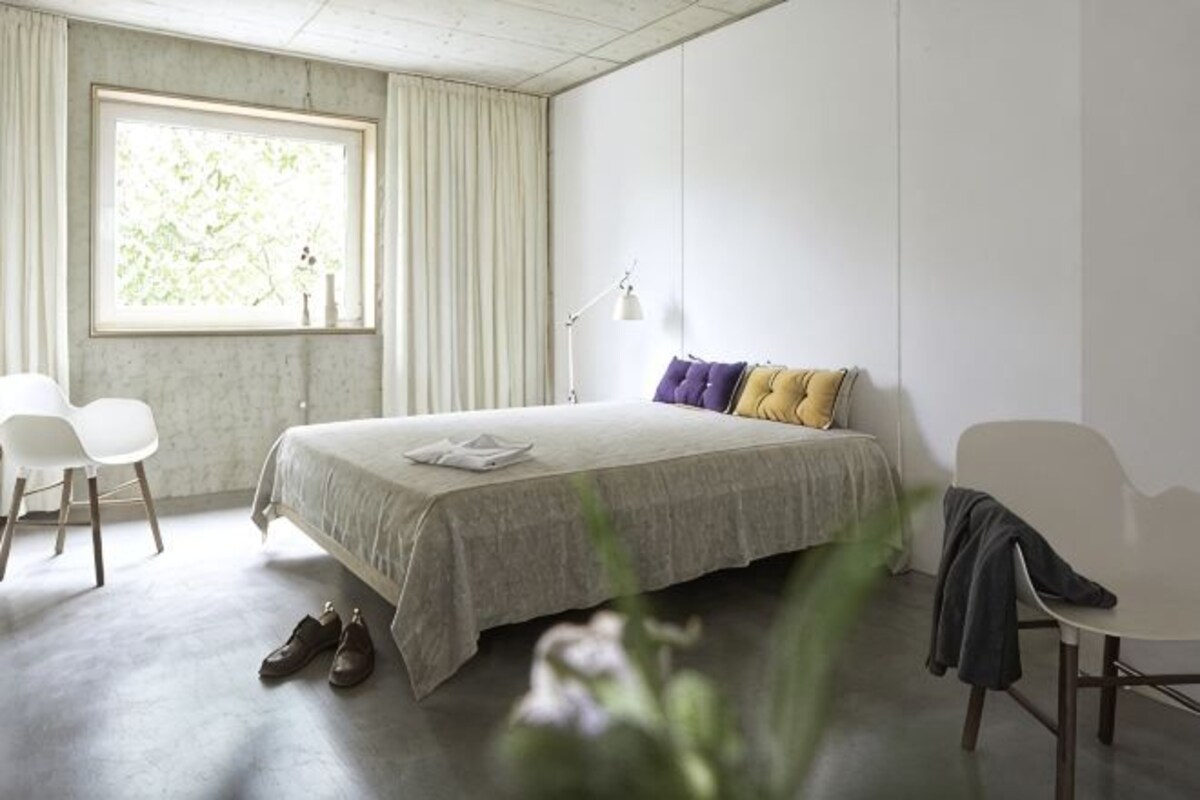 A bedroom with a bed, two chairs, a window, and a desk.