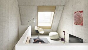 A modern bathroom with a skylight, a white vanity, a chair, and a decorative wall piece. - ipartment Cologne Mülheim (Cologne)