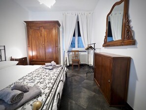 A hotel room with a bed, a wooden wardrobe, a radiator, a chair, and a window with curtains.