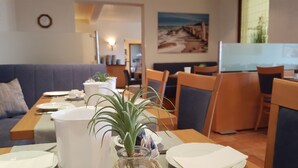 A dining area with a table set for two, a plant centerpiece, and a painting on the wall. - Hotel Vier Linden (Kellenhusen)
