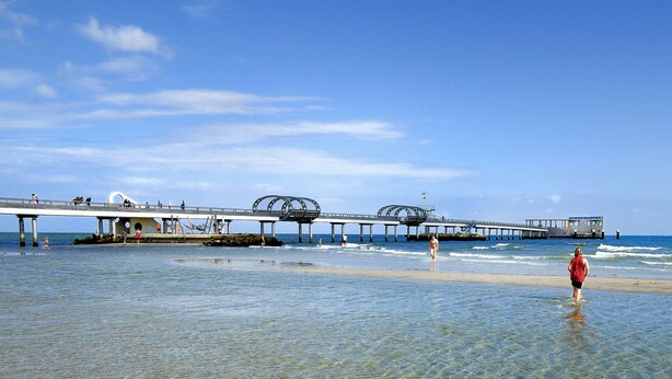 A pier extending into the water with people walking along it. - Hotel Vier Linden (Kellenhusen)