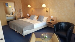 A hotel room with a large bed, two bedside lamps, a nightstand, a mirror, a black leather chair, and a small table with a glass. - Hotel Vier Linden (Kellenhusen)