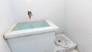 Une petite salle de bain carrelée, équipée d’une baignoire et de toilettes.