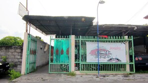 Un espace clos, délimité par une clôture verte, doté d’une entrée couverte et d’une enseigne publicitaire pour une entreprise.
