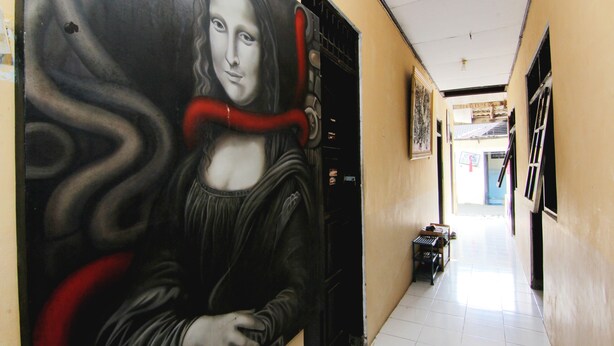 Un couloir orné d’une fresque représentant une femme en robe noire et en écharpe rouge, avec un sol carrelé et une porte dotée d’une poignée noire.