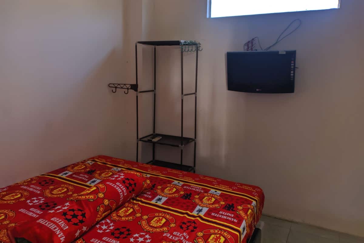 Una habitació amb un llit, una estantalla i un televisor de pantalla plana penjat a la paret.