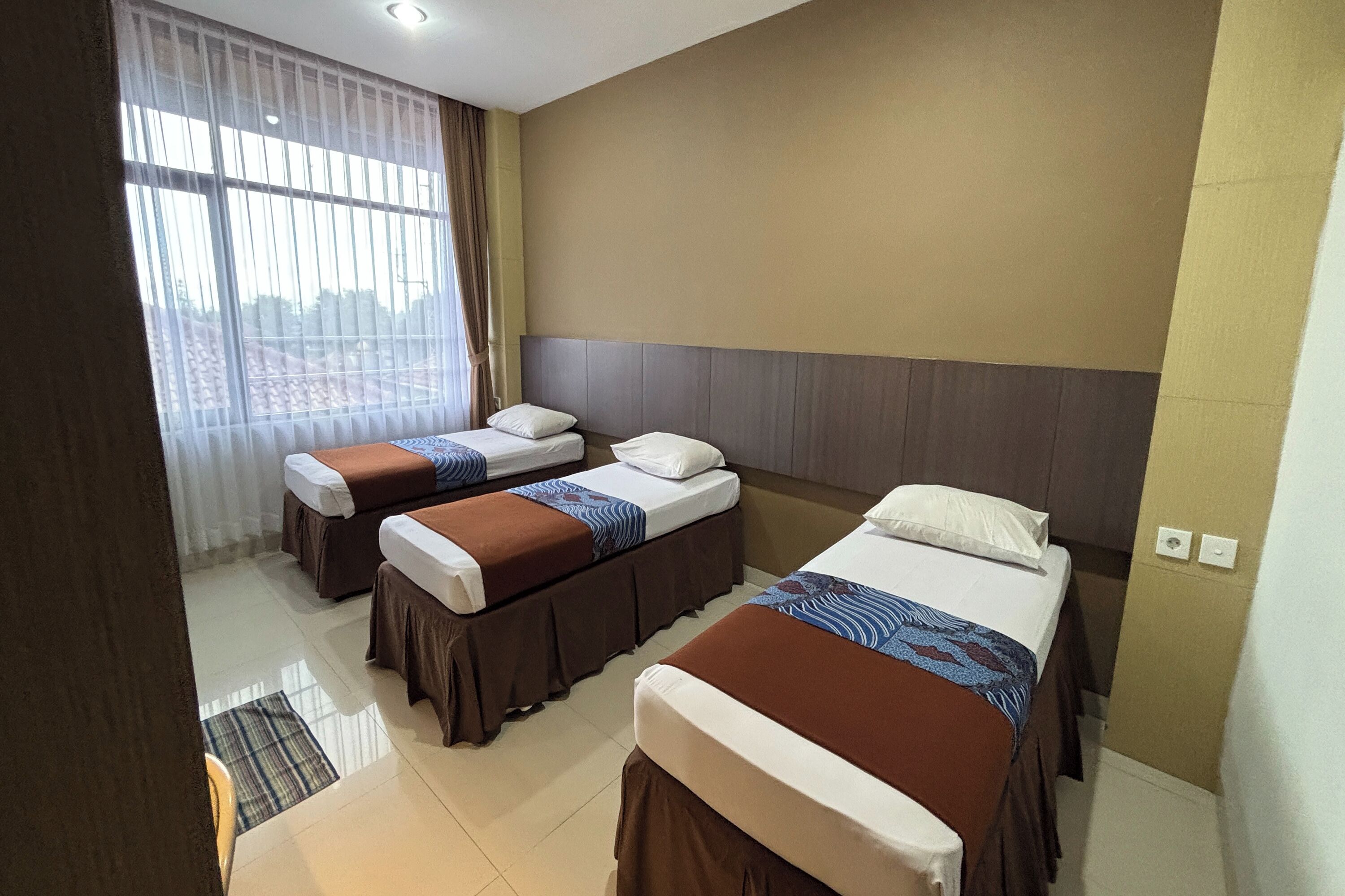 A hotel room with two single beds, a large window with sheer curtains, and a tiled floor.