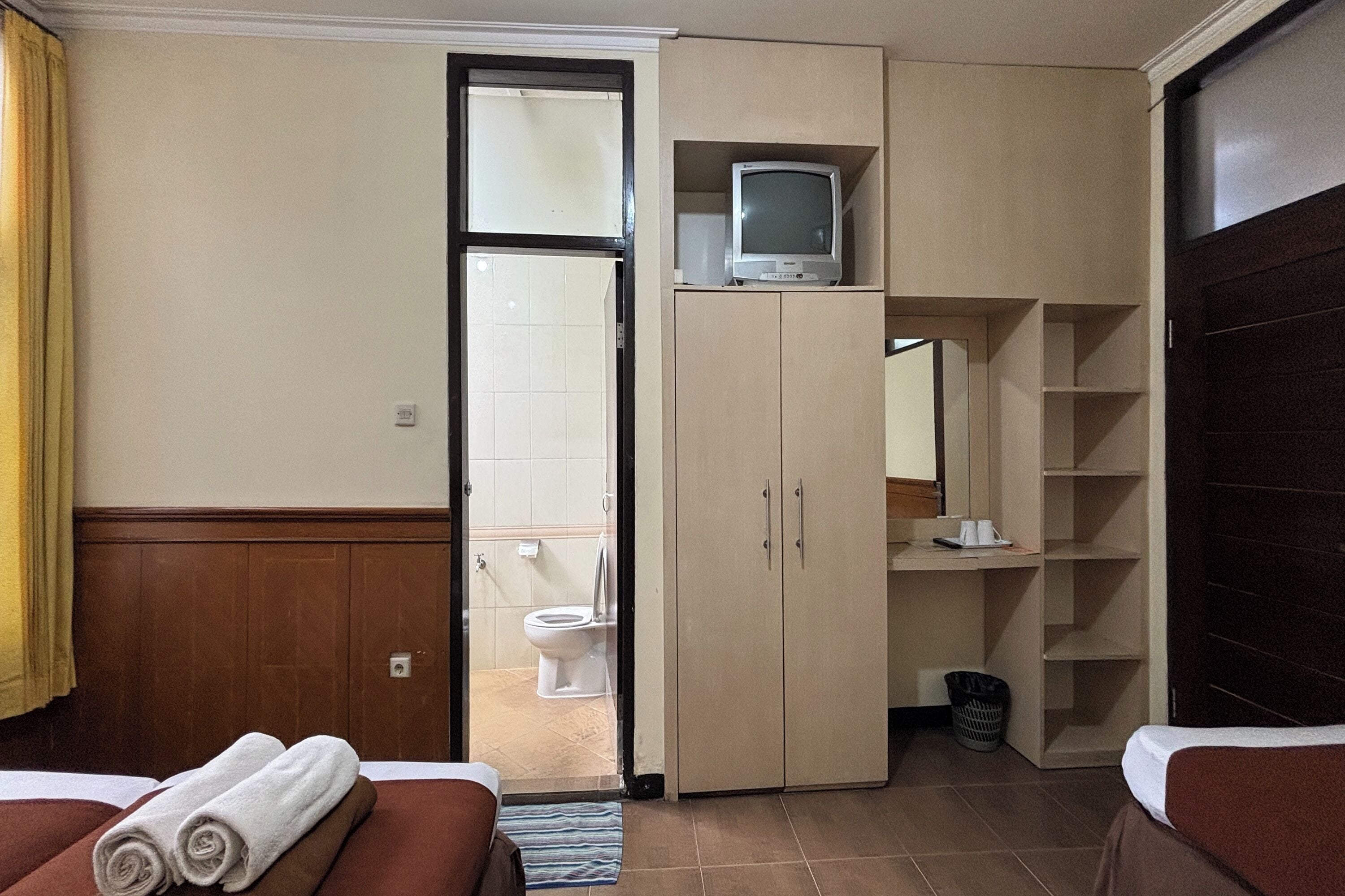 Habitación de hotel con dos camas, un televisor sobre una mesita, un baño visible a través de una puerta abierta y un cesto de basura.