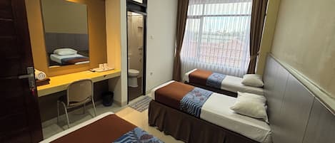 Ein Hotelzimmer mit zwei Betten, einem Schreibtisch, einem Stuhl, einem Spiegel und einem Fenster mit Vorhängen.