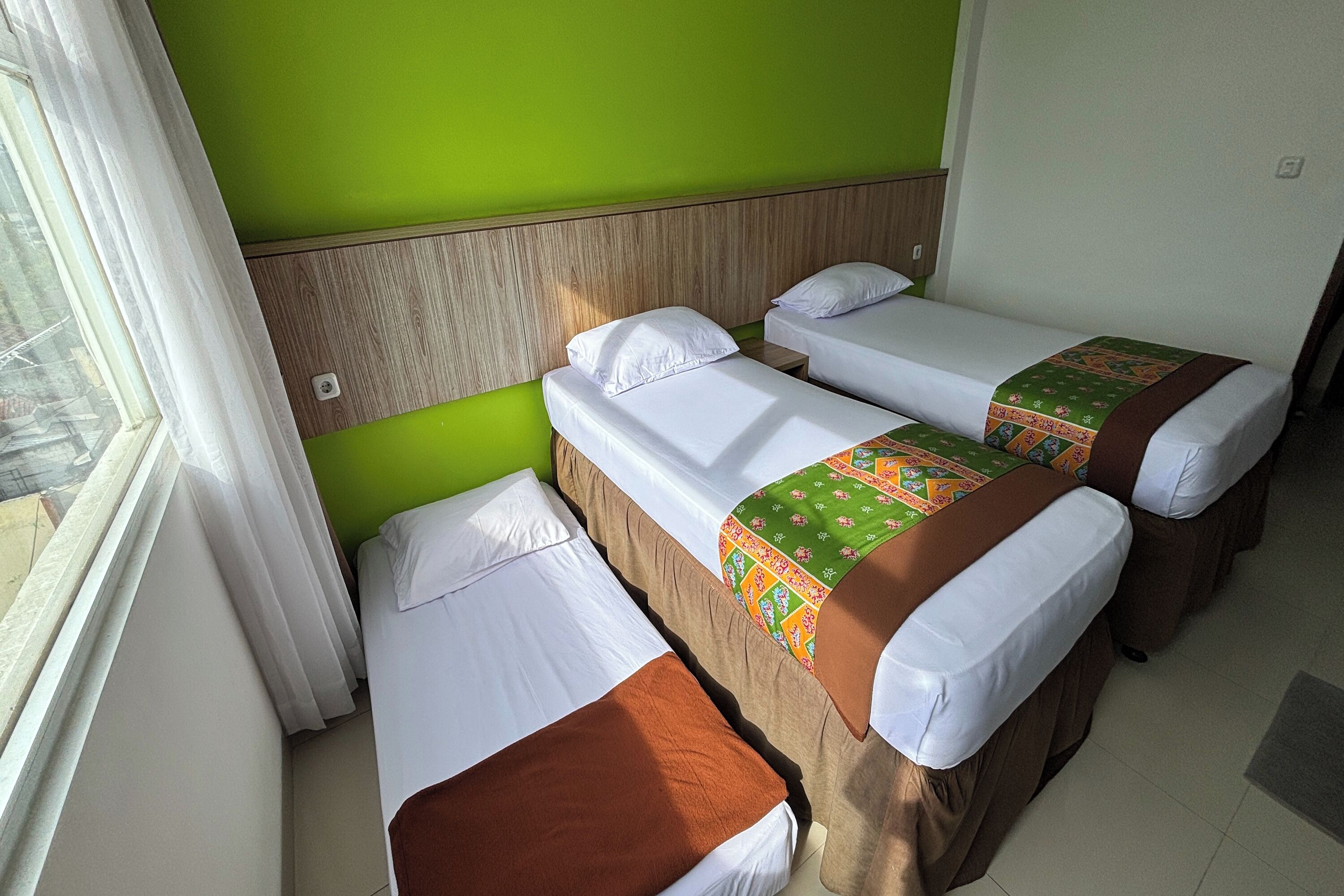 A room with two single beds, each with white linens and brown bedspreads. The room has green walls and a wooden headboard.