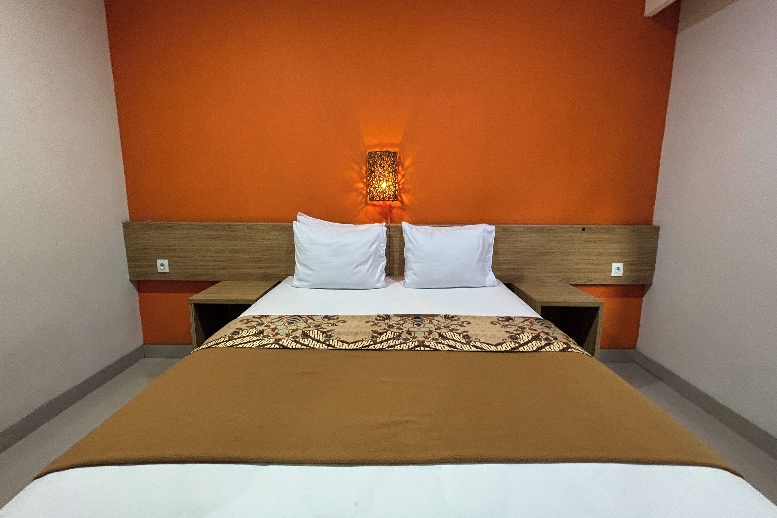Una habitación de hotel con una cama, dos mesitas de noche, una lámpara de pared y un plaid estampado.