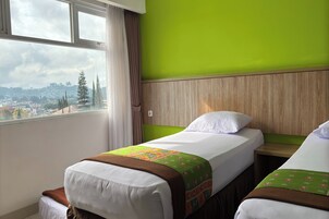 Una habitación de hotel con dos camas, un ventanal con cortinas y vistas a un paisaje urbano.