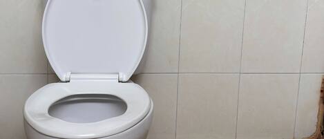 Un inodoro en un baño con azulejos color beige y piso de tonos claros.