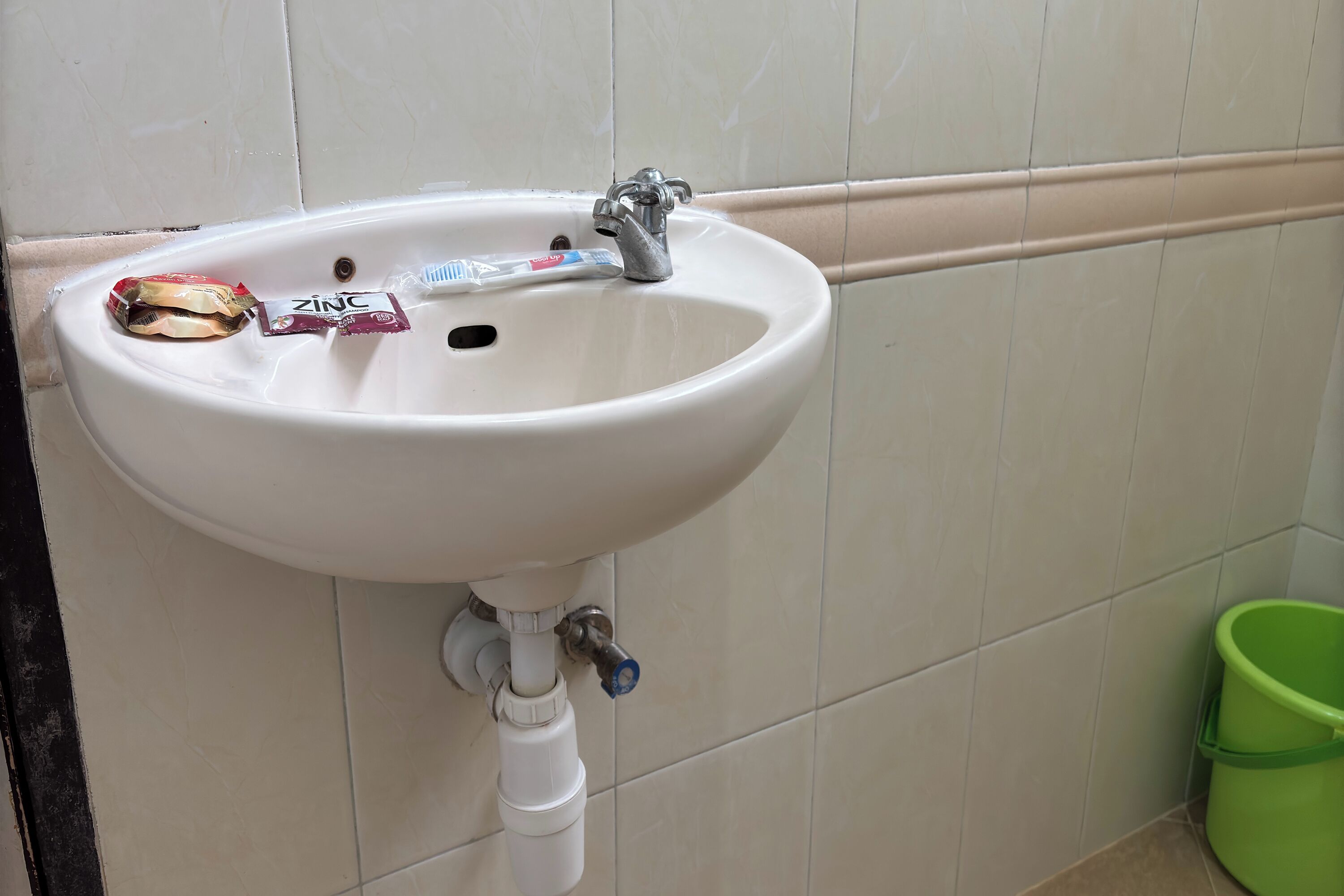 A white bathroom sink with a faucet, a green trash bin, and a toothbrush.
