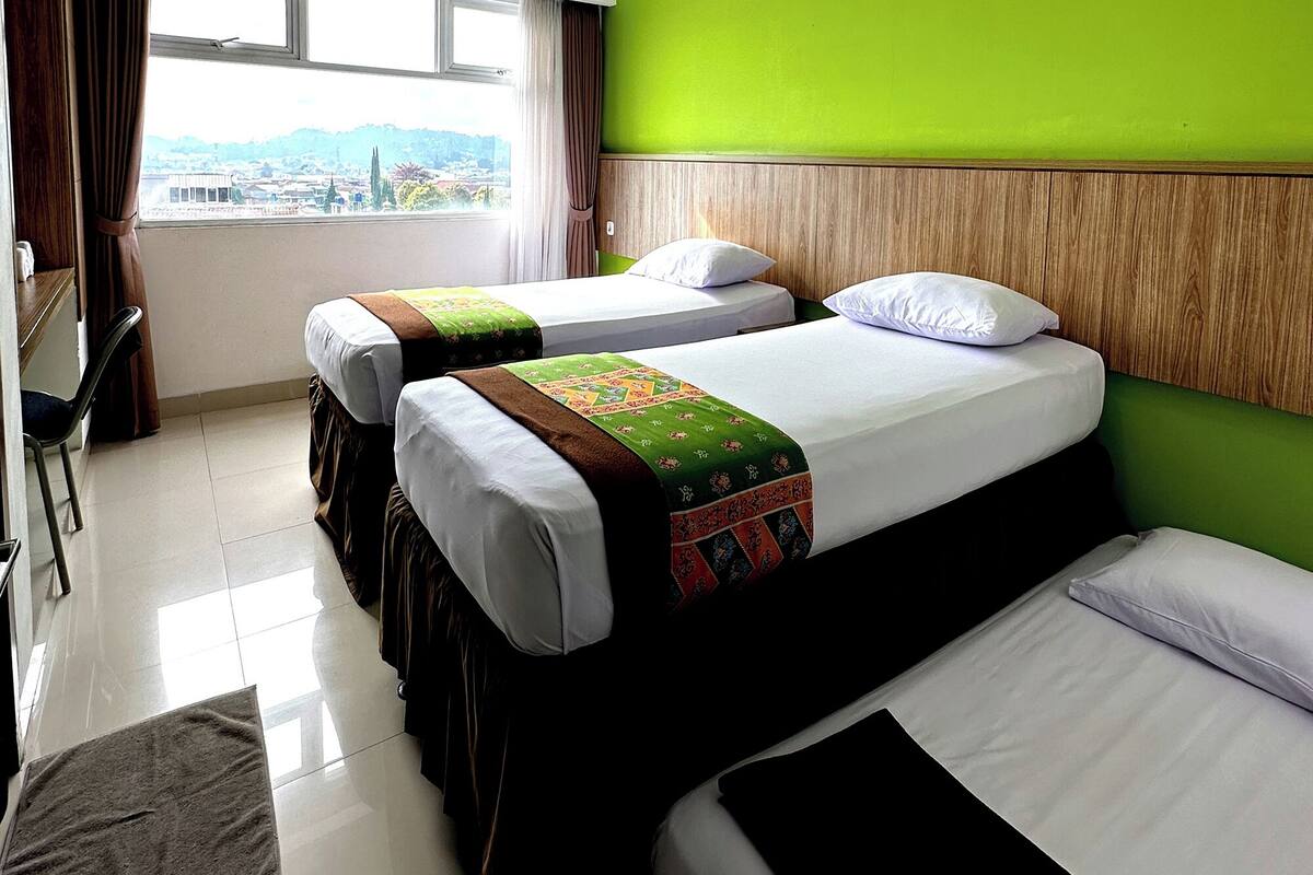 A hotel room with two beds, a desk, and a window with a city view.