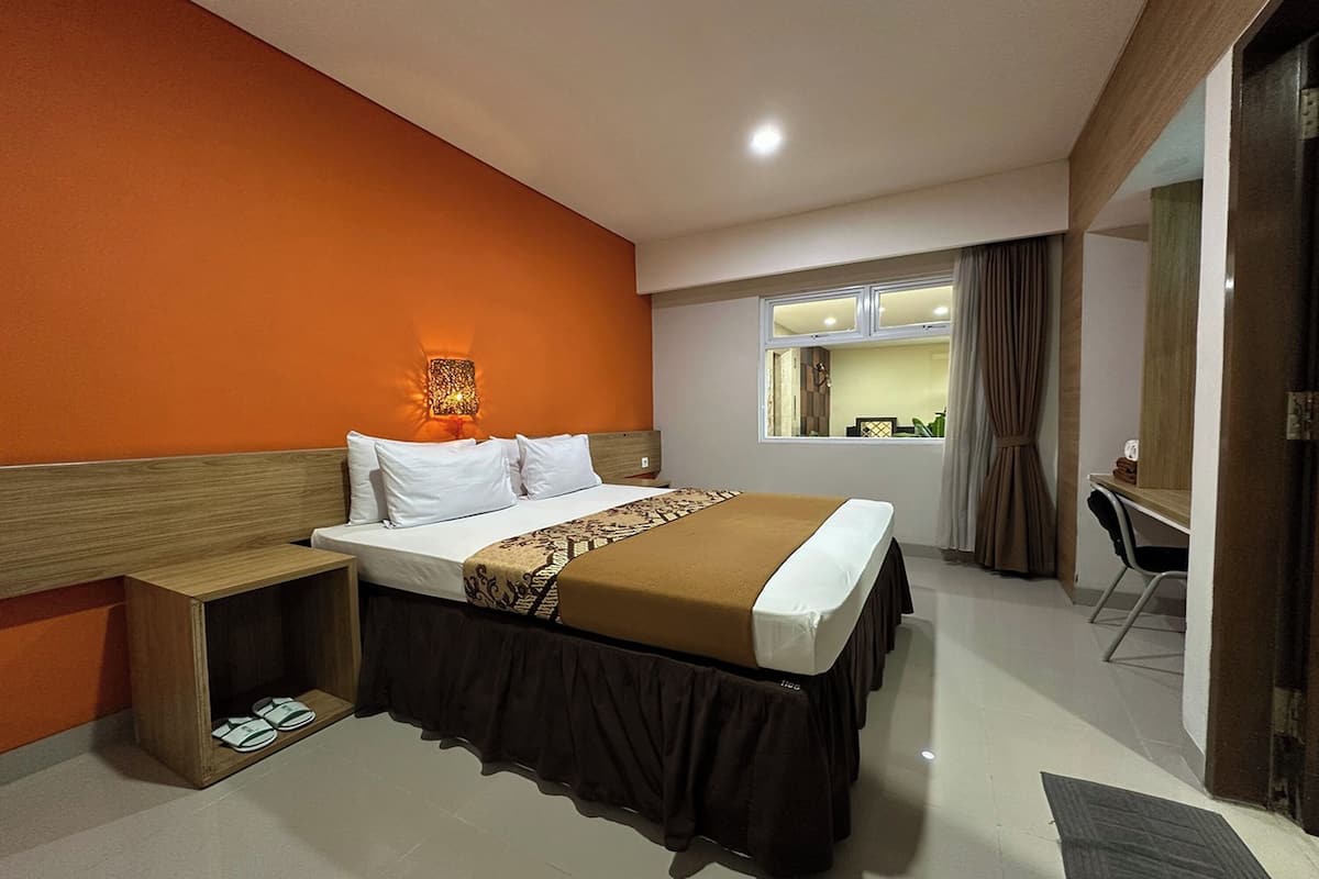 A hotel room with a bed, bedside table, and a desk with a chair.