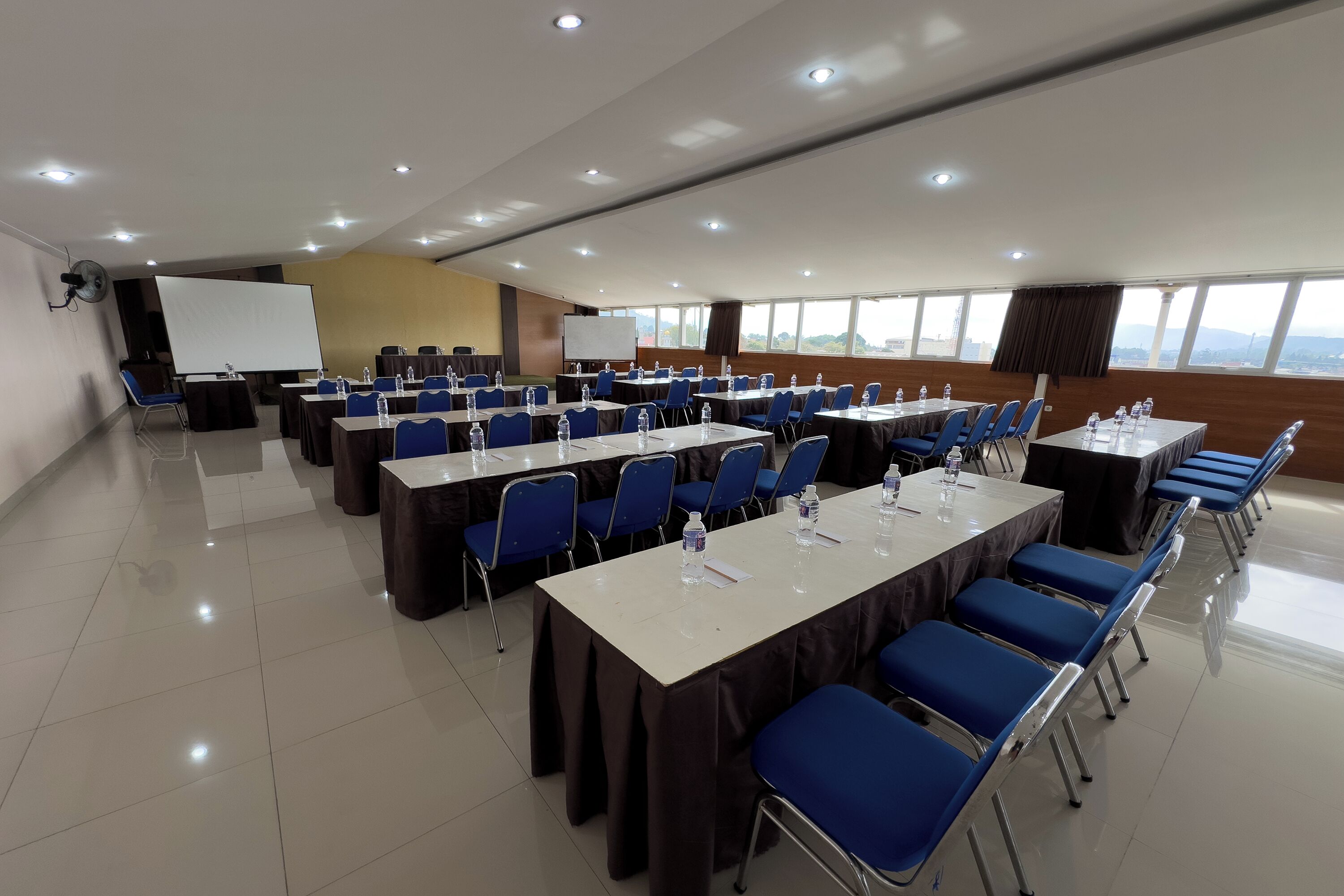 Un salón de conferencias con mesas y sillas, una pizarra y una pantalla de proyector.