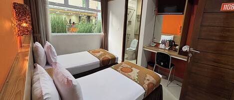 A hotel room with two beds, a desk, a chair, a TV, and a bathroom visible through an open door.