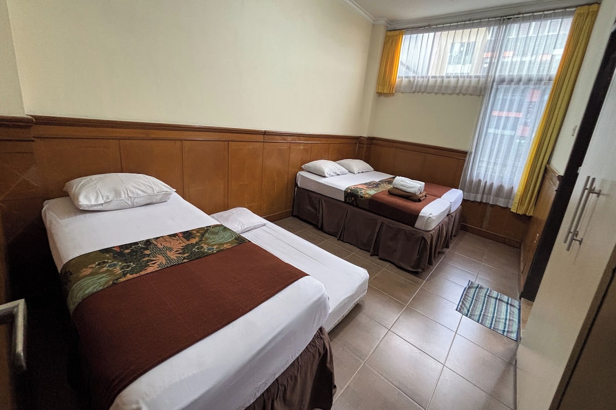 A hotel room with two beds, a window with curtains, and a tiled floor.