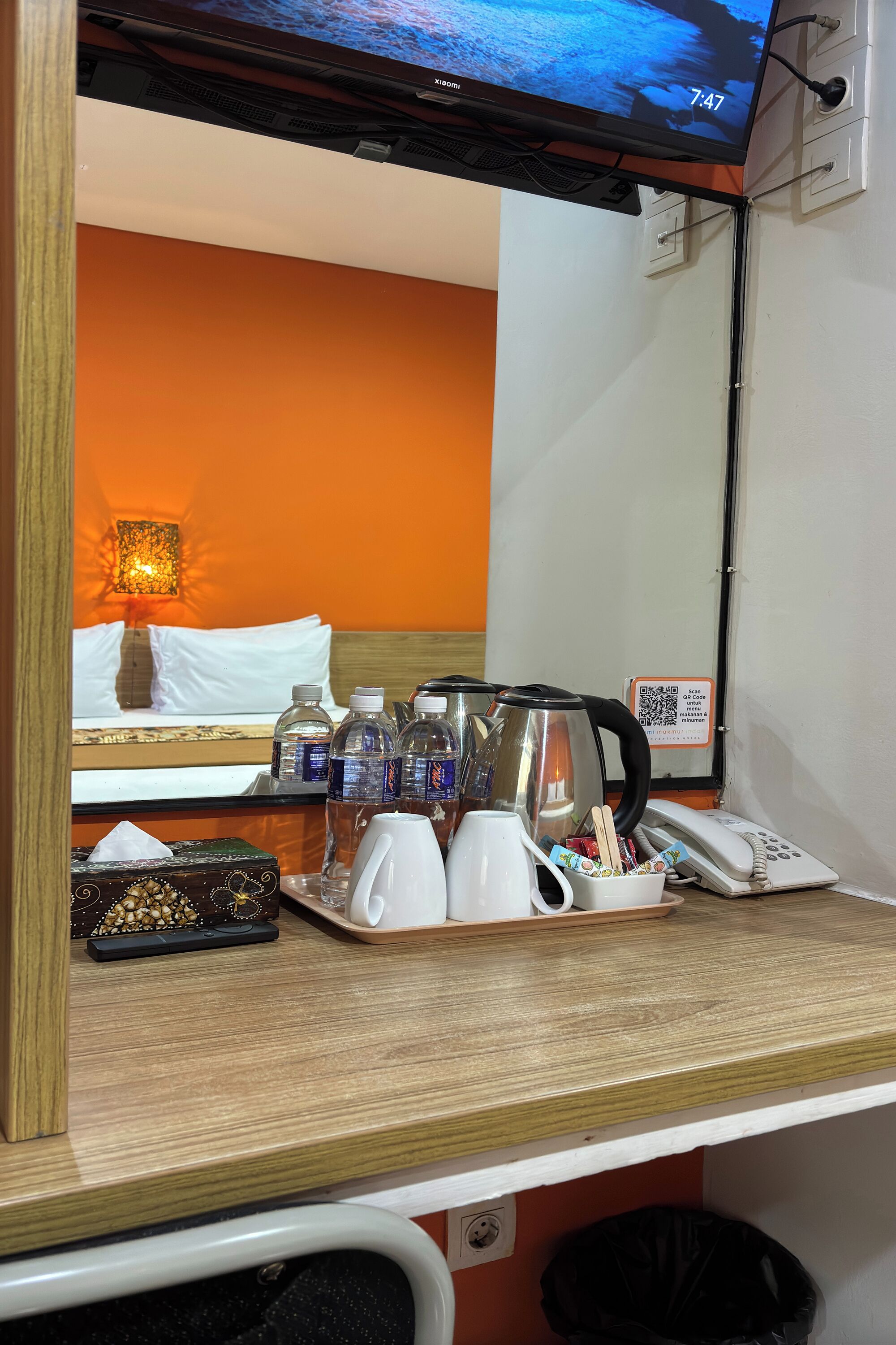 A hotel room with a bed, a bedside table with a kettle, cups, and a phone.