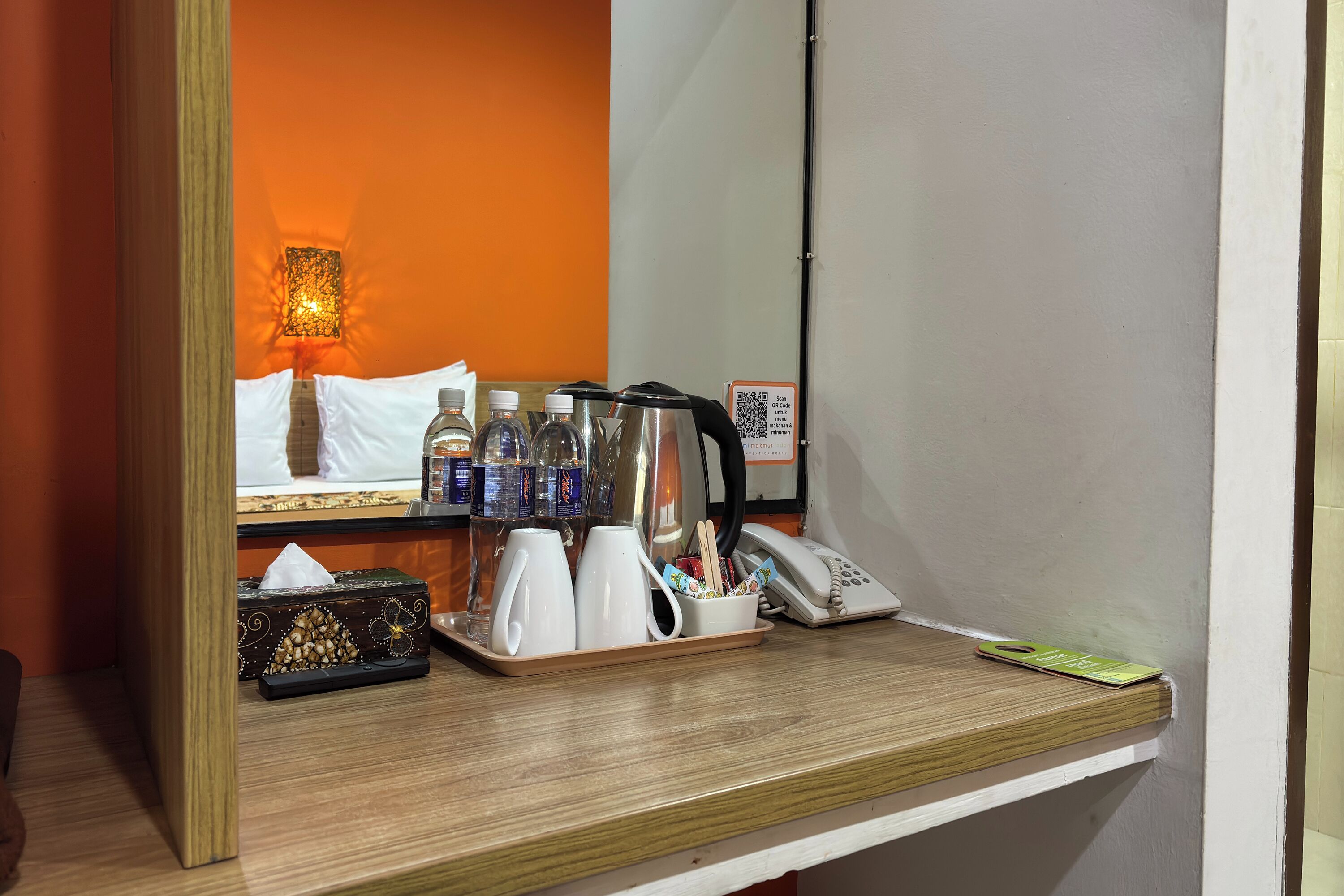 A hotel room's reception area with a wooden counter, a tray with toiletries, a telephone, and a mirror reflecting the room.