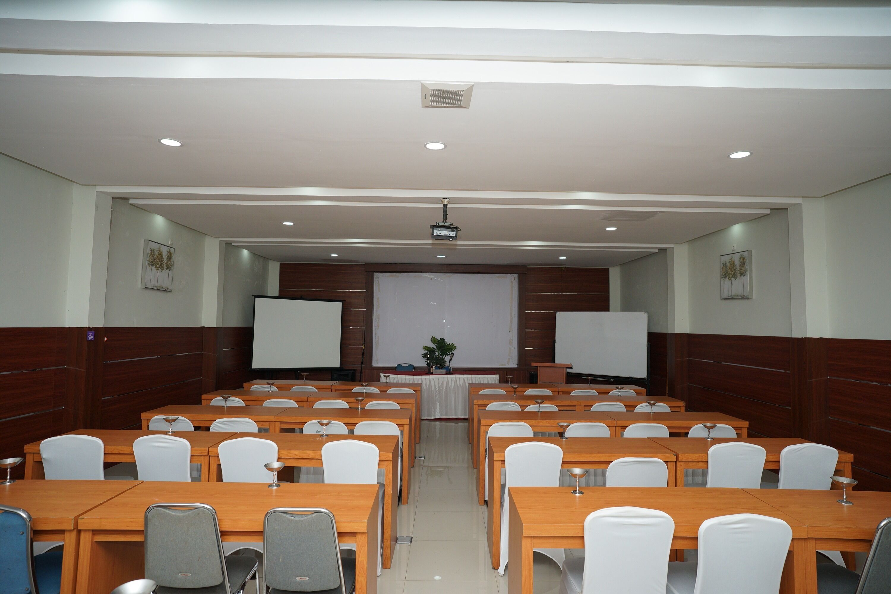 Un salón de conferencias con varias mesas y sillas, una pantalla de proyector y una pizarra.