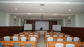 Un salón de conferencias con varias mesas y sillas, una pantalla de proyector y una pizarra.