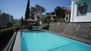 Una piscina con un muro de piedra y un pabellón, rodeada de vegetación y edificios.