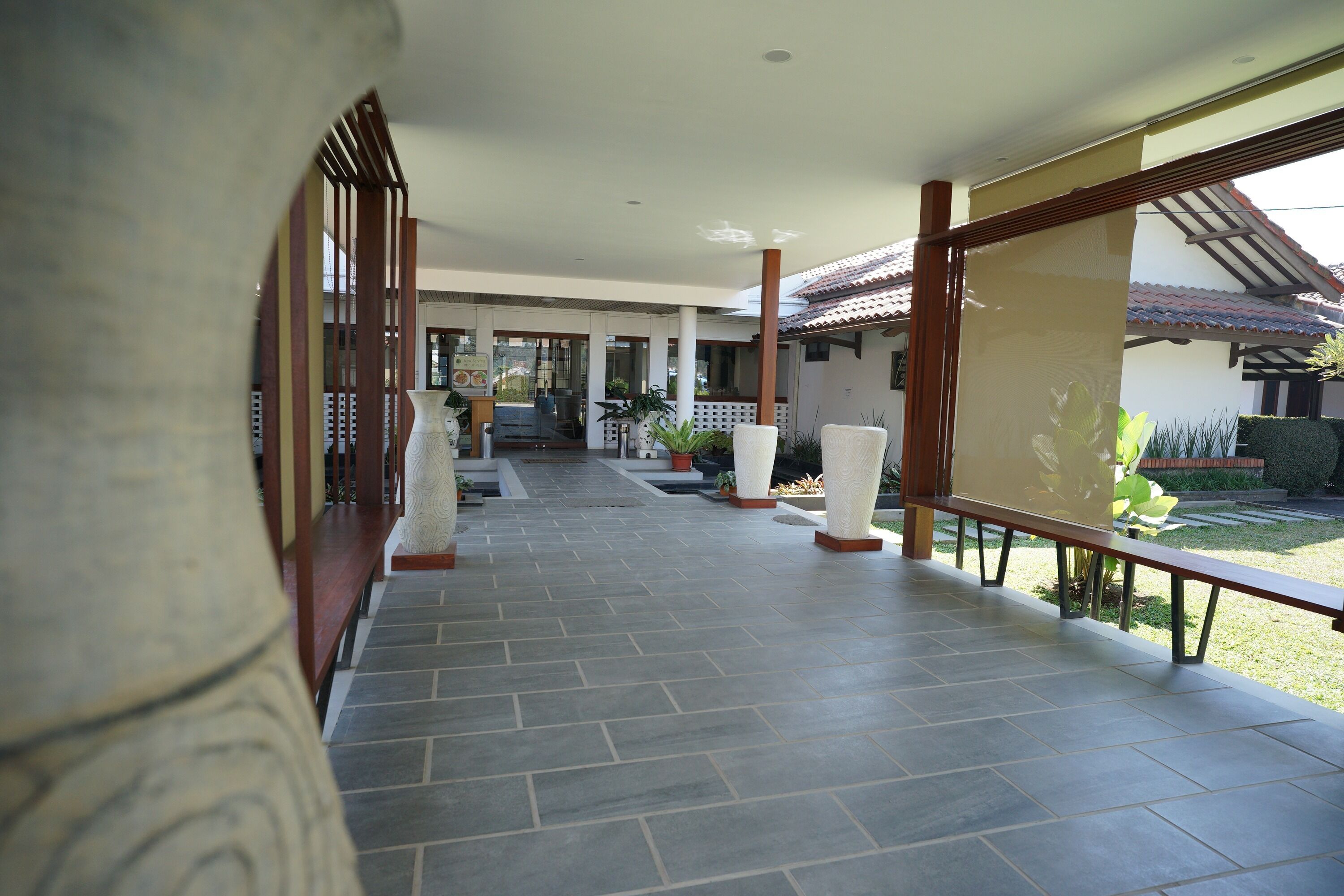 A covered outdoor corridor with tiled flooring, wooden railings, and potted plants.