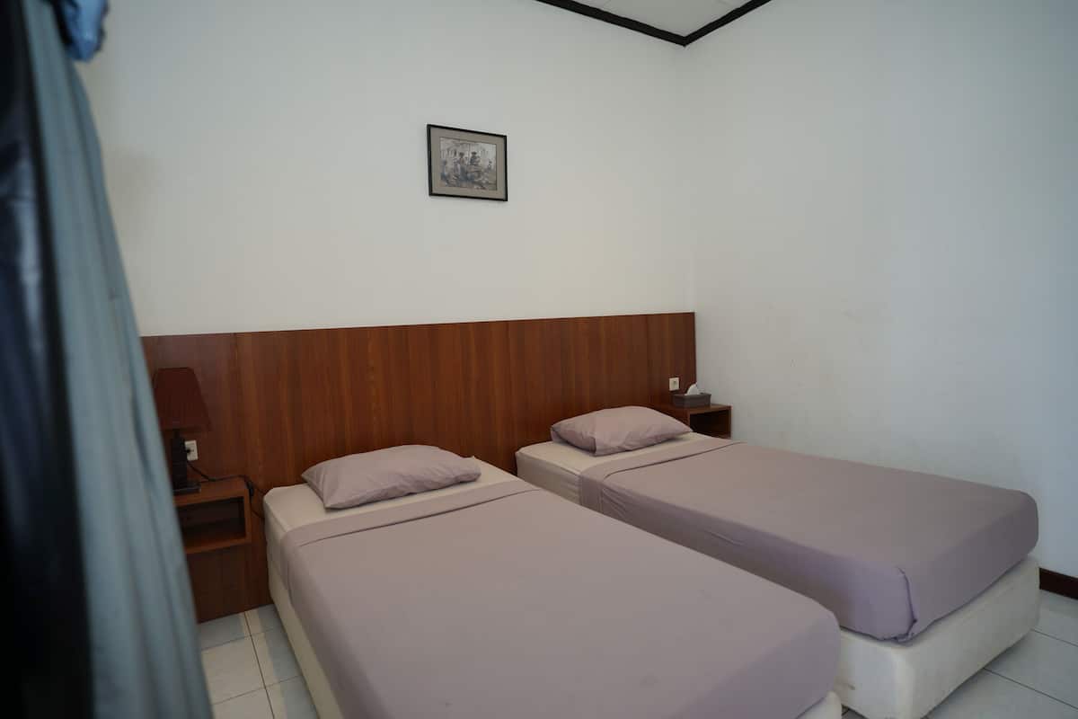A room with two single beds, wooden headboards, a nightstand with a lamp, and a framed picture on the wall.