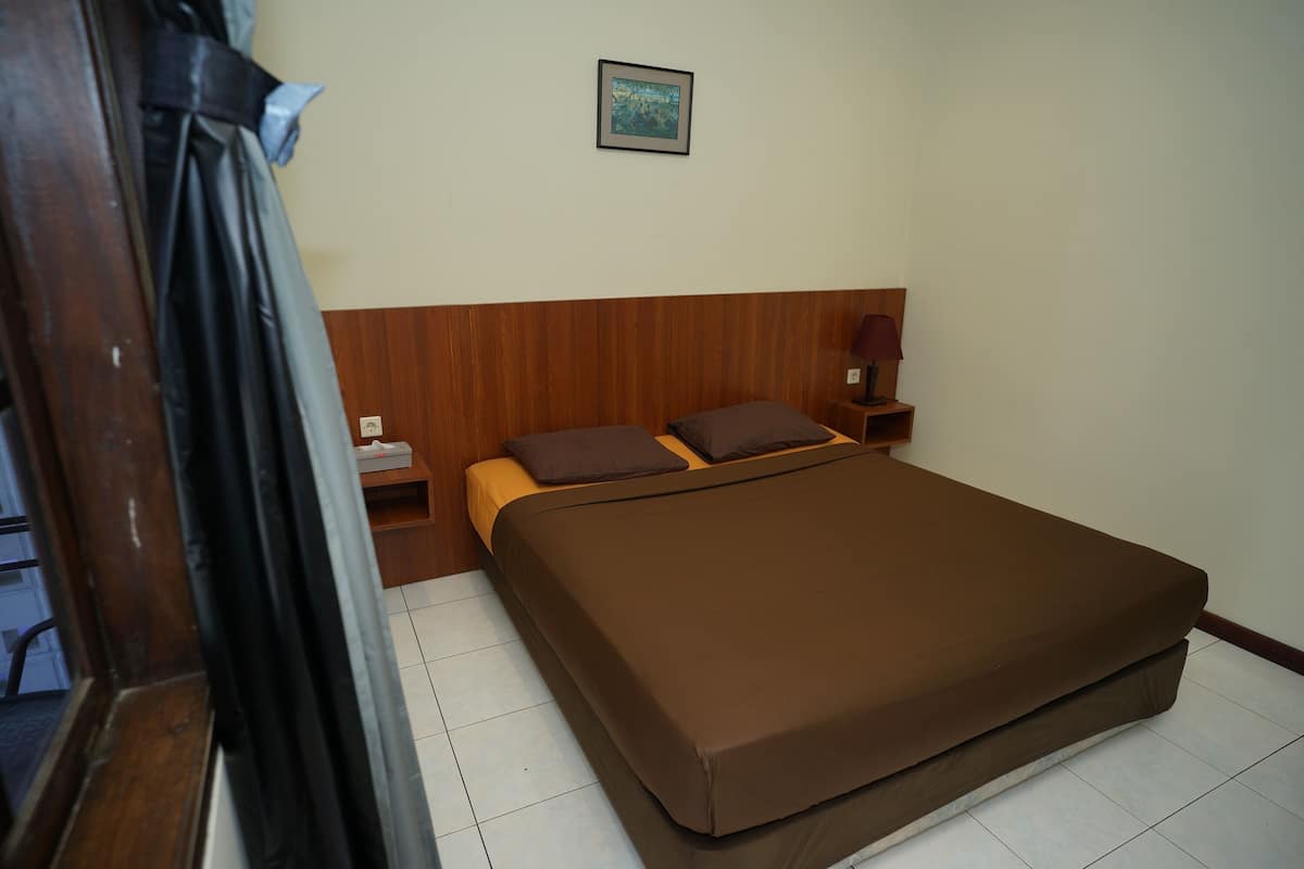 A bedroom with a wooden headboard, a bed with brown bedding, a nightstand with a lamp, and a framed picture on the wall.