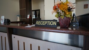 Un mostrador de recepción con un cartel que dice 'RECEPTION', un florero y un certificado enmarcado en la pared.