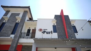 Un hotel llamado 'Puri' con una fachada moderna, un balcón y una entrada visible.