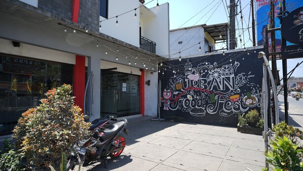 Vista de una calle con una motocicleta estacionada frente a un edificio con un mural que dice 'URBAN Food Fest'.
