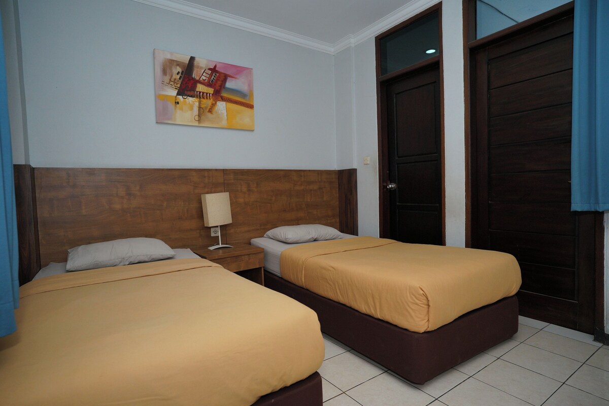 A hotel room with two beds, a wooden headboard, a nightstand, a lamp, and a painting on the wall.