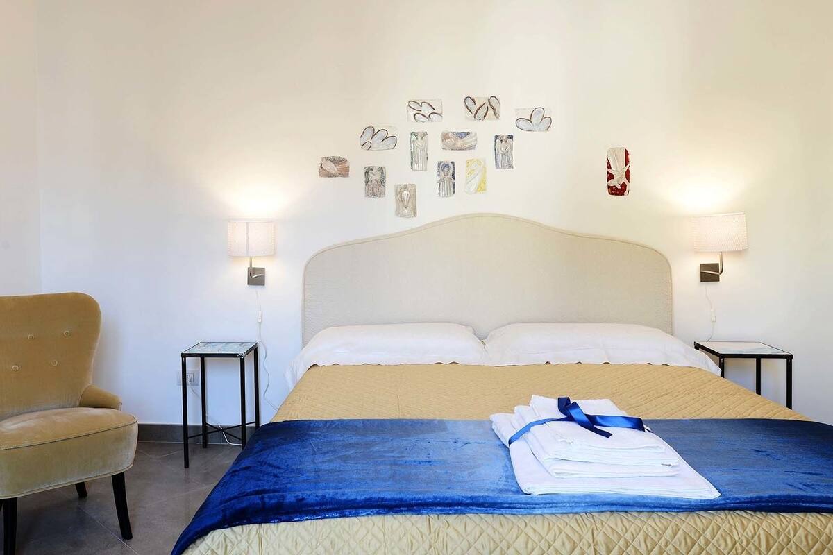 A hotel room with a bed, a chair, and artwork on the wall.