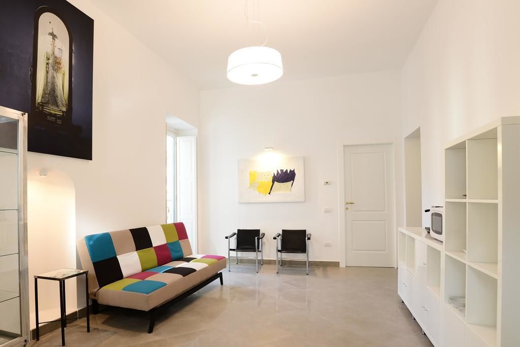 Una sala de estar moderna con un sofá colorido, dos sillas negras, un mueble blanco y una obra de arte enmarcada en la pared.