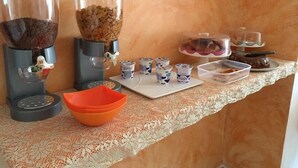 A buffet setup with coffee and cereal dispensers, a tray of yogurt cups, and a cake display. - Dragonfly B&B (Trapani)