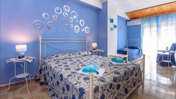 A bedroom with a bed, two bedside tables, a wall art piece, and a window with curtains. - Dragonfly B&B (Trapani)
