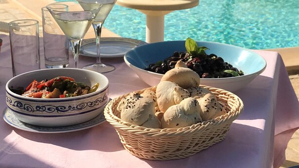 A poolside table with a bowl of olives, a basket of bread, and a martini glass.
