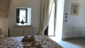 A bedroom with a bed, a window with curtains, a radiator, and a framed picture on the wall.