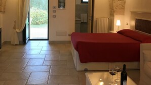 A bedroom with a stone ceiling, a bed with a red blanket, a bedside table with a wine bottle and glasses, and a bathroom visible through an open door.