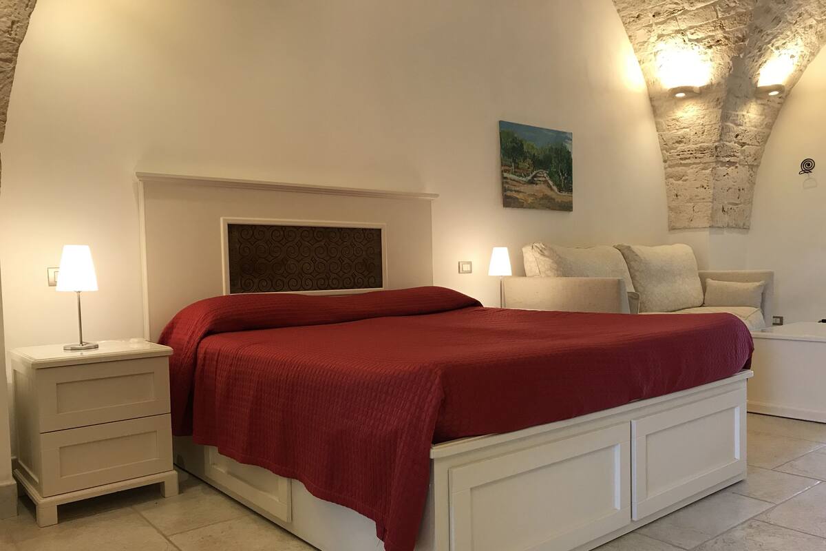 Ein Schlafzimmer mit Bett, Nachttischen, einem Kopfteil, einem Gemälde und einer Steindecke.
