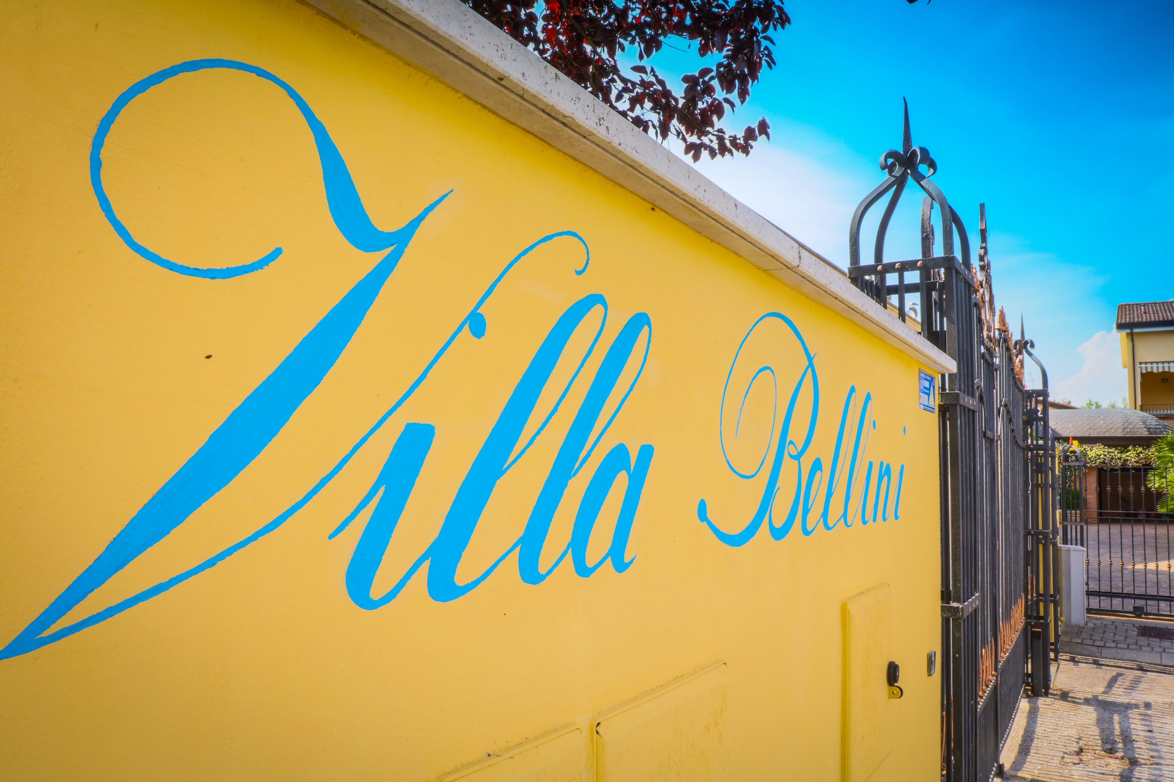 En gul vägg med orden ”Villa Bellini” skrivna med blå kursivstil.